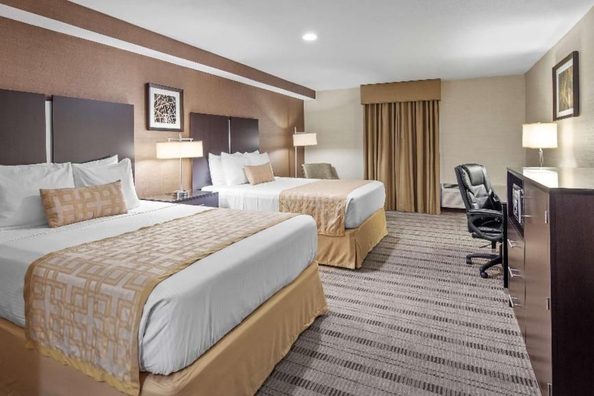 A hotel room with two beds, a desk, a chair, and a large window with curtains.