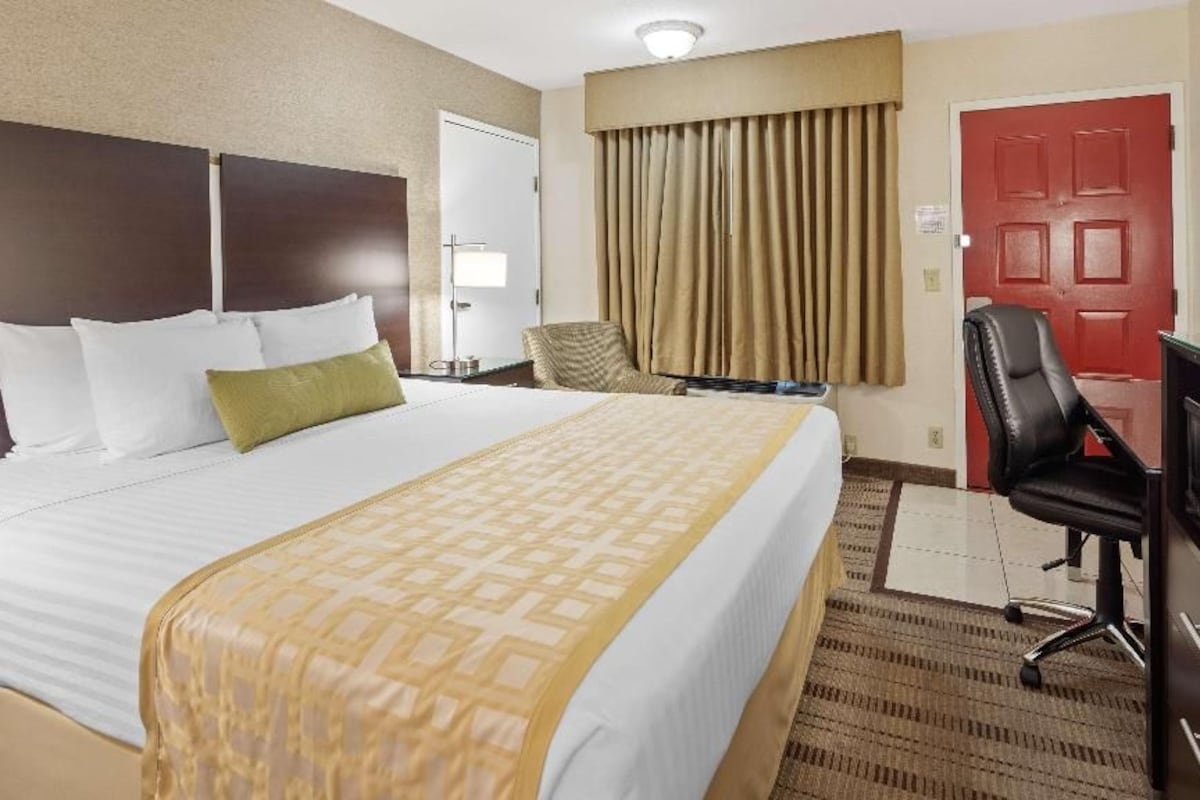 A hotel room with a large bed, a desk, a chair, a television, and a red door.