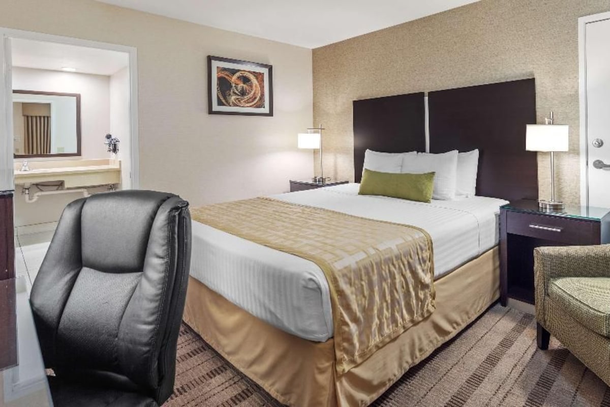 A hotel room with a bed, a chair, a nightstand, a lamp, and a mirror.