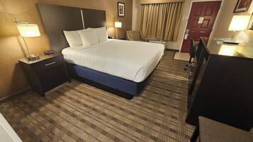 Una habitación de hotel con una cama grande, un escritorio, una silla, una lámpara y una puerta.