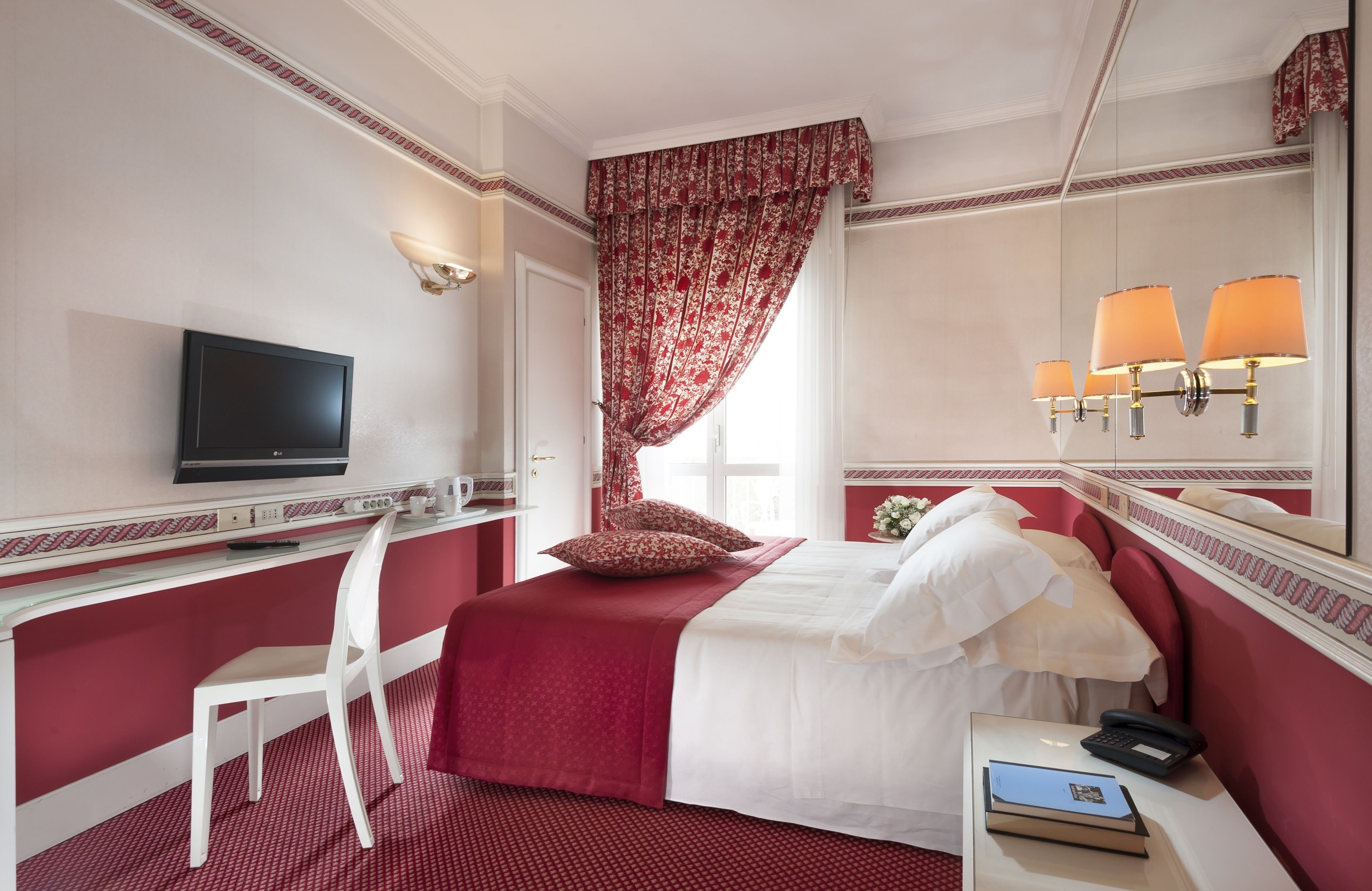 Habitación de hotel con cama, escritorio, silla, televisor, lámpara y teléfono.