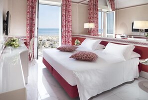Habitació d'hotel amb un llit gran, una taula de treball i vista al mar.