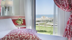A hotel room with a bed, a small table with a vase of flowers, and a view of the sea through large windows. - Hotel Milton (Rimini)