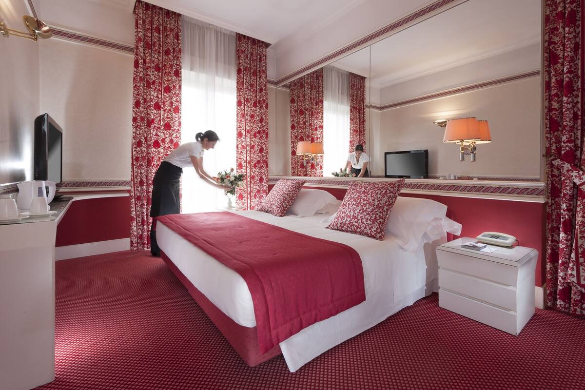A hotel room with a large bed, a bedside table, a nightstand, a mirror, and a television.