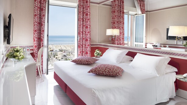 A hotel room with a large bed, a desk with a chair, and a view of the sea. - Hotel Milton (Rimini)