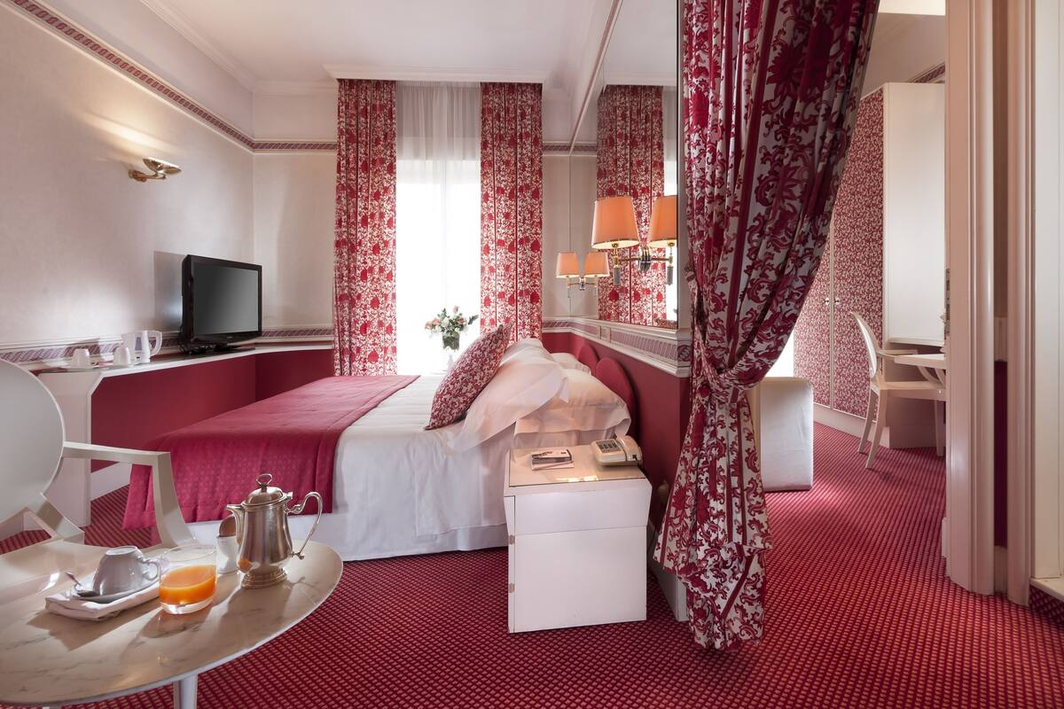 A hotel room with a bed, bedside table, TV, and a breakfast setup.
