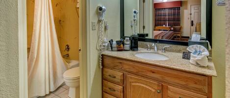 A bathroom with a shower, toilet, wooden vanity, and a large mirror.