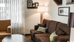 A living room with a brown sofa, a round coffee table, a lamp, and a chair. There are framed pictures on the wall. - Sleep Inn Summersville - New River Gorge Area (Summersville)