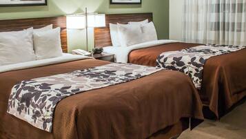 A hotel room with two beds, a nightstand, a lamp, and framed pictures on the wall.