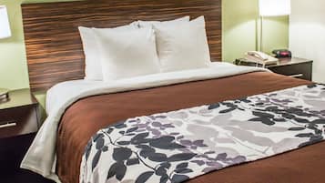A neatly made bed with a brown bedspread and a floral-patterned blanket, a wooden headboard, a bedside table with a lamp, and a framed picture on the wall.