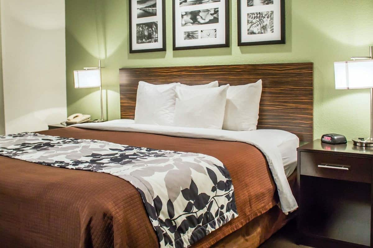 A hotel room with a bed, a nightstand, a lamp, and three framed pictures on the wall.