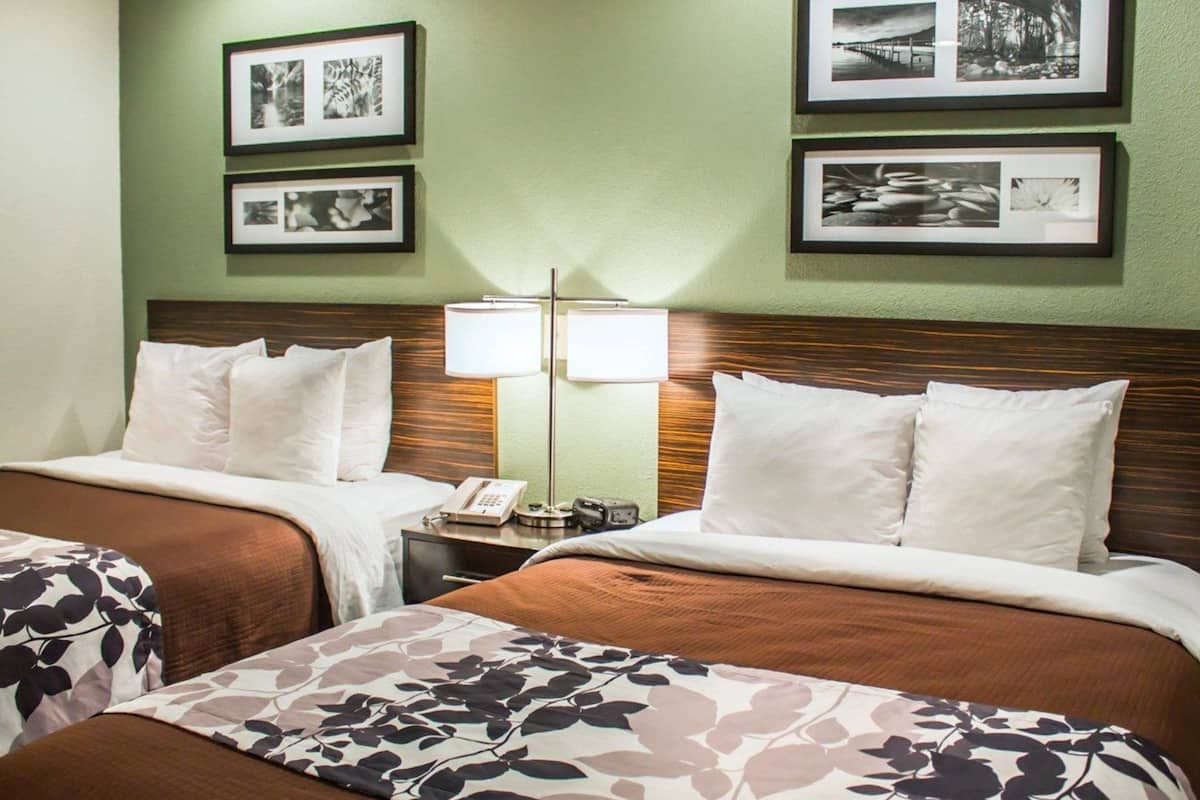 A hotel room with two beds, a nightstand with a lamp, and framed pictures on the wall.