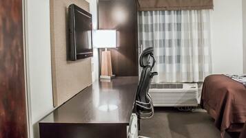 Habitación de hotel con escritorio, silla, cama, televisión, lámpara y aire acondicionado.