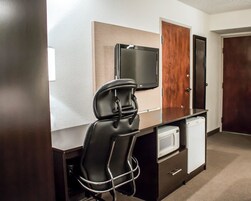 A compact hotel room with a kitchenette, a flat-screen TV mounted on the wall, a wooden door, and a small refrigerator.