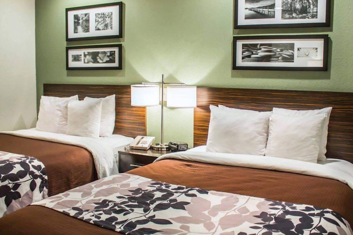 A hotel room with two beds, a nightstand with a lamp, and framed pictures on the wall.