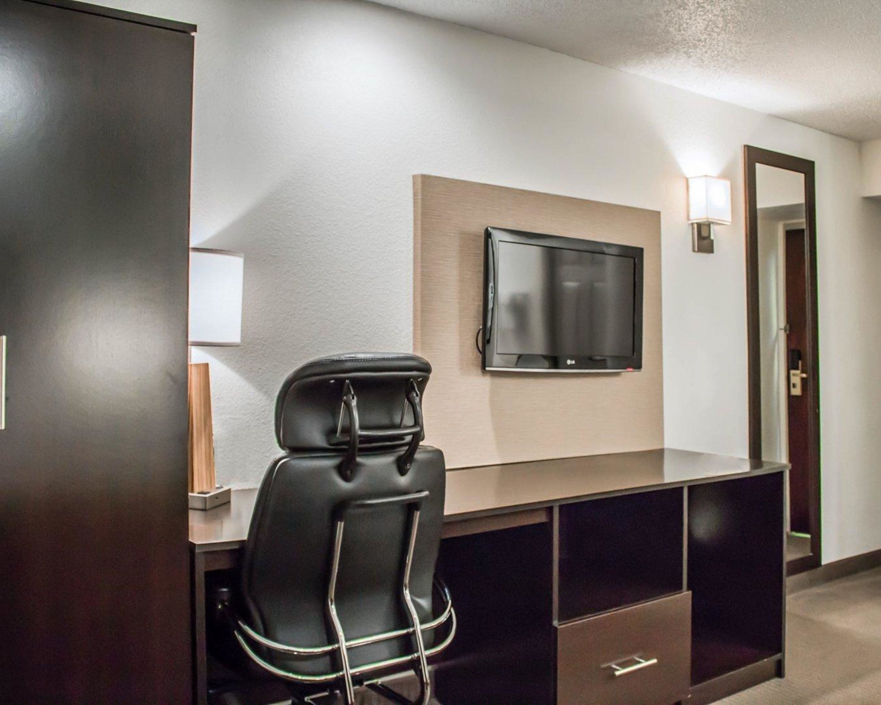 Habitación de hotel con televisor de pantalla plana montado en la pared, un sillón de cuero negro, un escritorio con cajones y una lámpara en la mesita de noche.