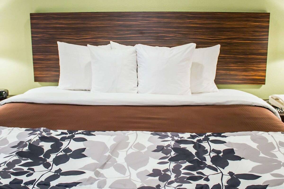A hotel room with a bed, a headboard, and a floral-patterned bedspread.
