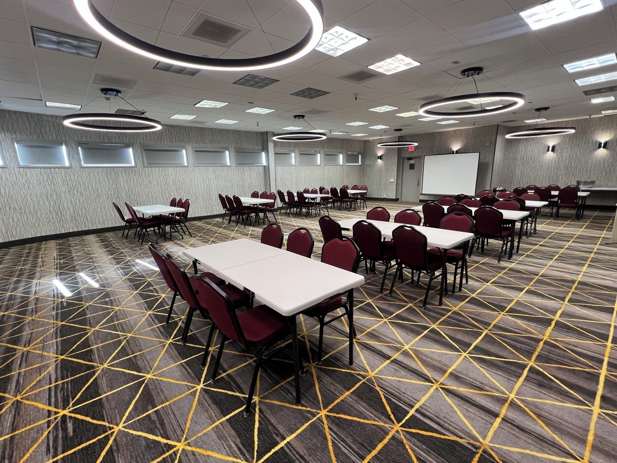 Un salón de conferencias con mesas y sillas, una pantalla de proyector y una alfombra estampada.