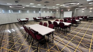 A conference room with tables and chairs, a projector screen, and a patterned carpet.