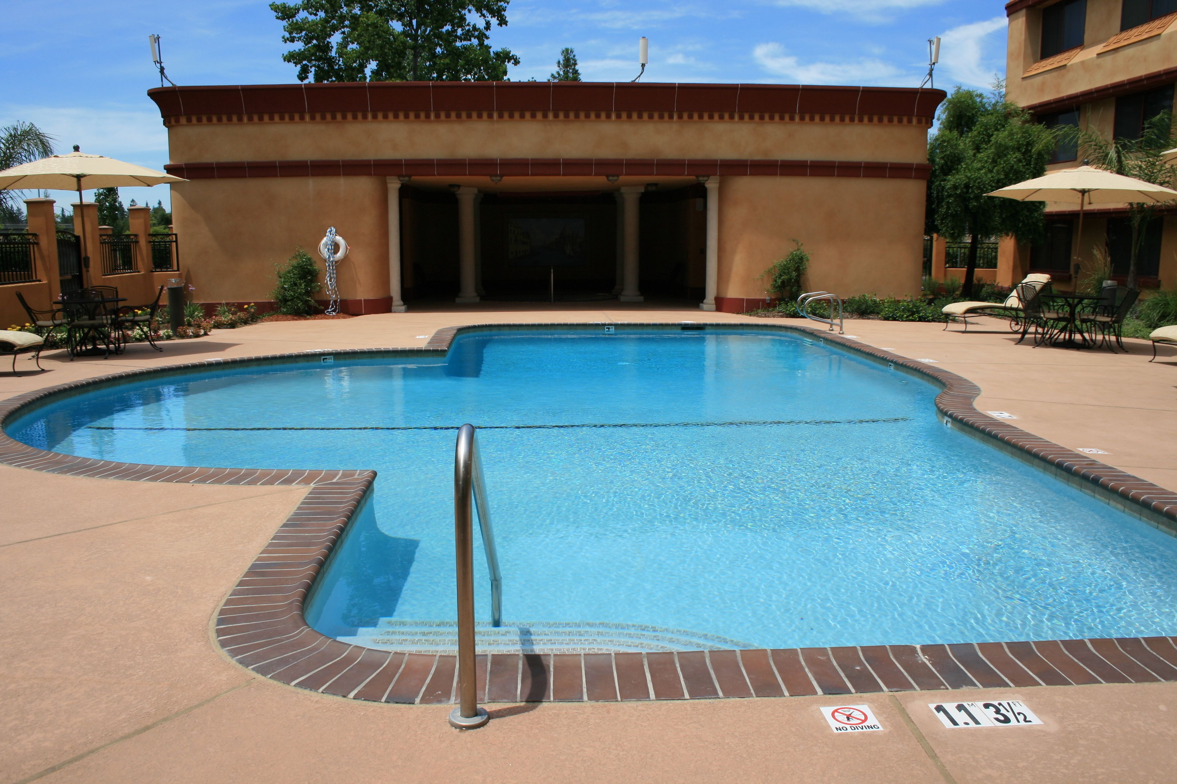 Une piscine avec un panneau indiquant qu’il est interdit de plonger, des chaises longues et des parasols.
