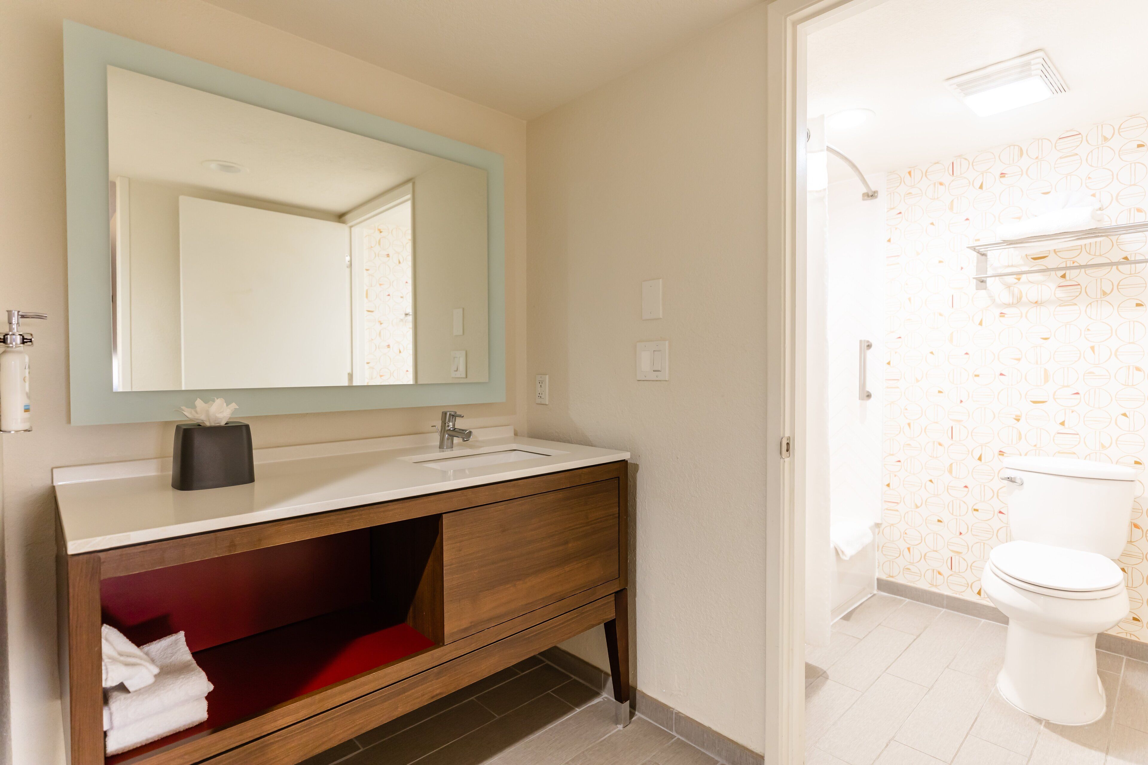 A bathroom with a wooden vanity, a large mirror, and a white toilet.