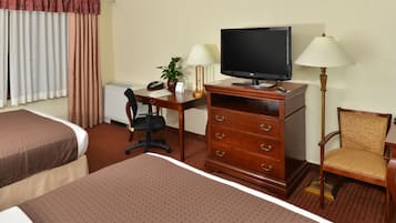 Una camera d'albergo con due letti, una scrivania con televisore, una sedia, una lampada e una pianta.