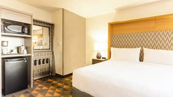 A hotel room with a bed, a microwave, a mini-fridge, a nightstand, and a patterned floor.