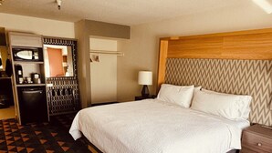 A hotel room with a bed, a desk, a chair, a small table, and a mirror.