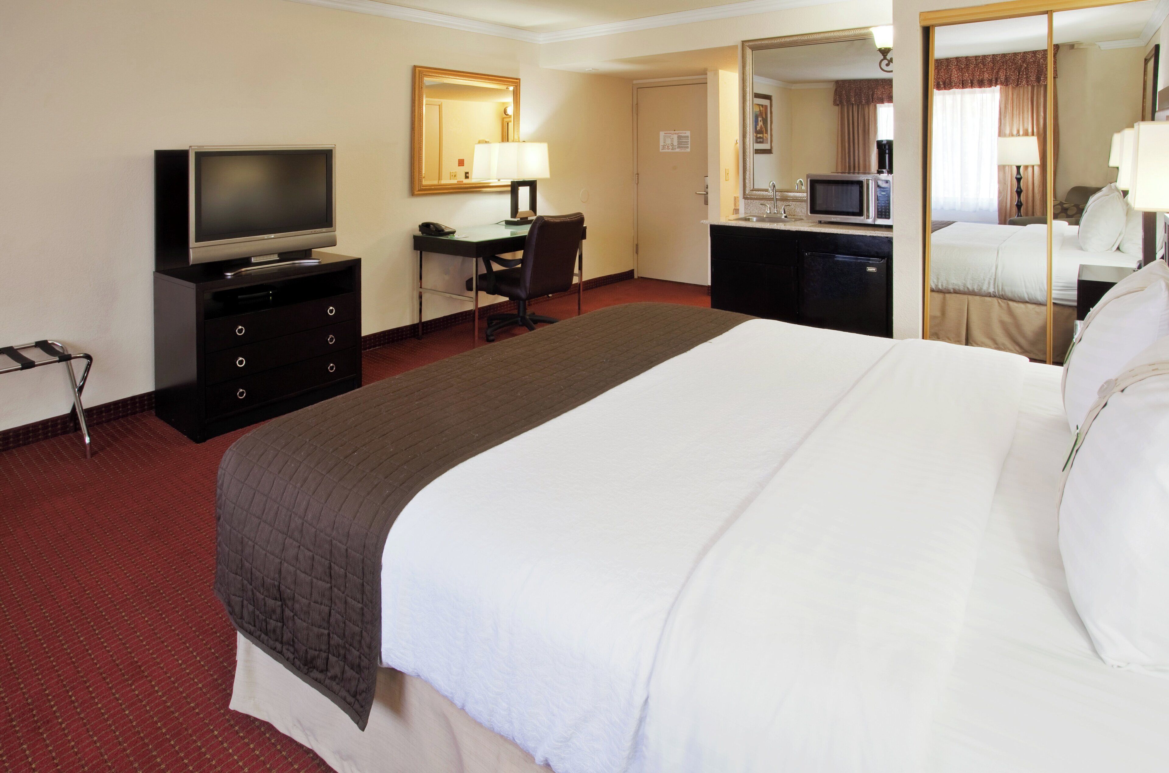 Une chambre d’hôtel comprenant un lit, un bureau avec une chaise, une télévision, un four à micro-ondes et un petit réfrigérateur.