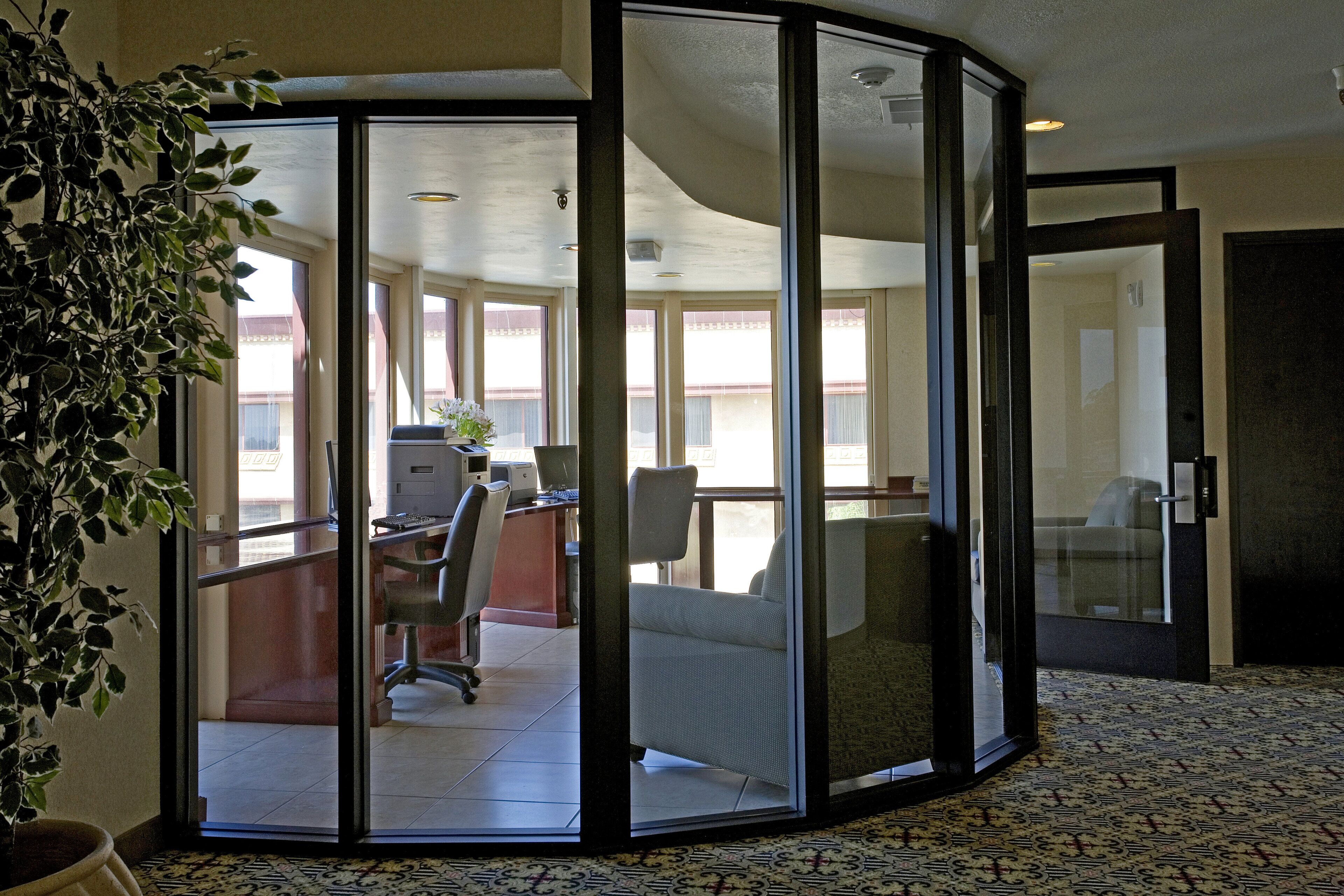 Un bureau d’angle équipé d’un bureau, d’une chaise et d’un ordinateur, avec une plante en pot et une vue sur un bâtiment à l’extérieur.