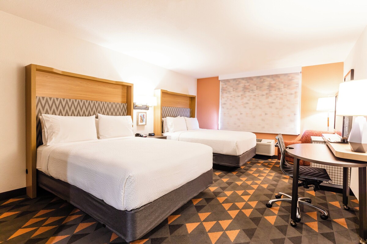 A hotel room with two beds, a desk, and a chair.