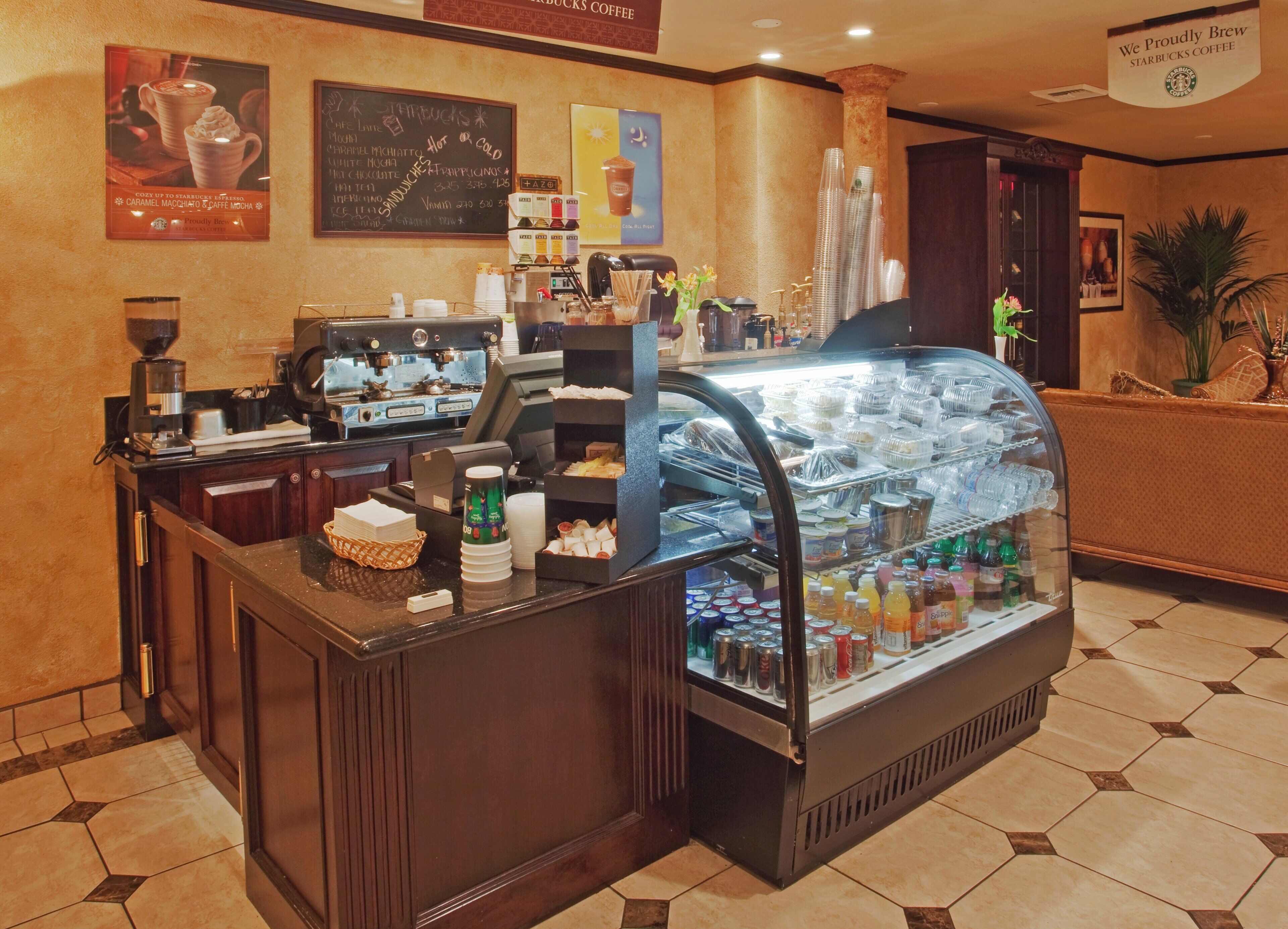 A coffee shop counter with a coffee machine, a glass display case with beverages, and a menu board on the wall.
