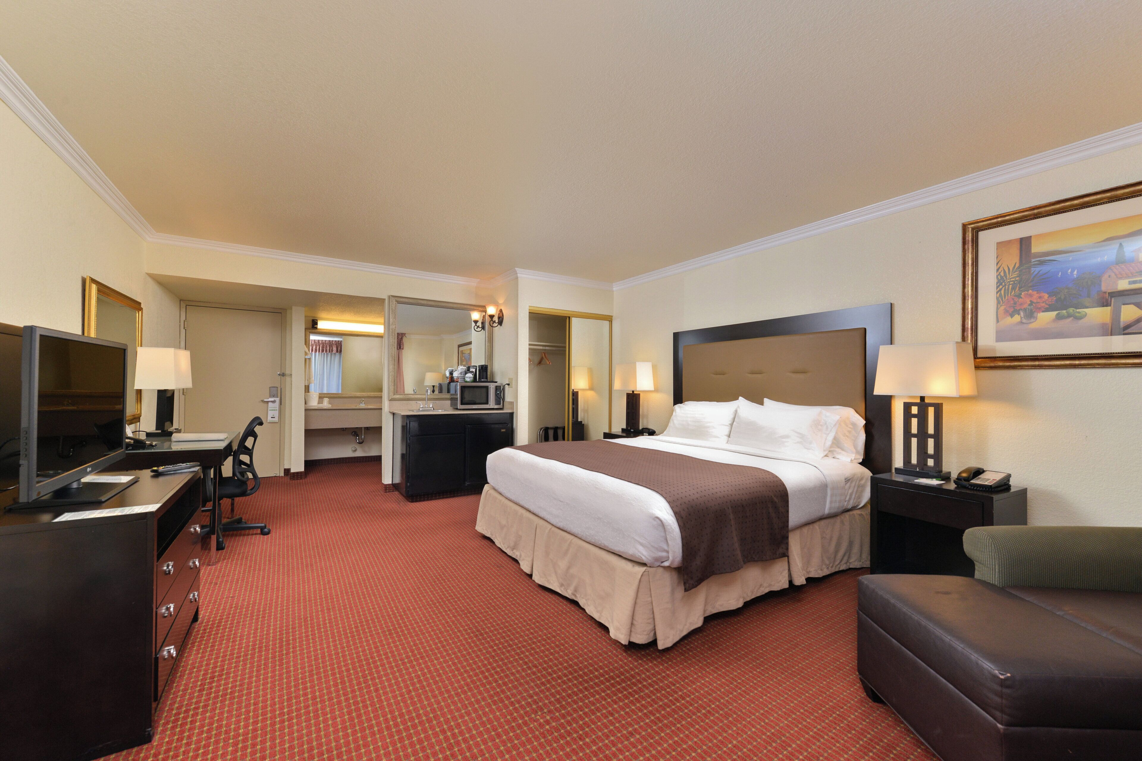 A hotel room with a bed, desk, chair, and a television.