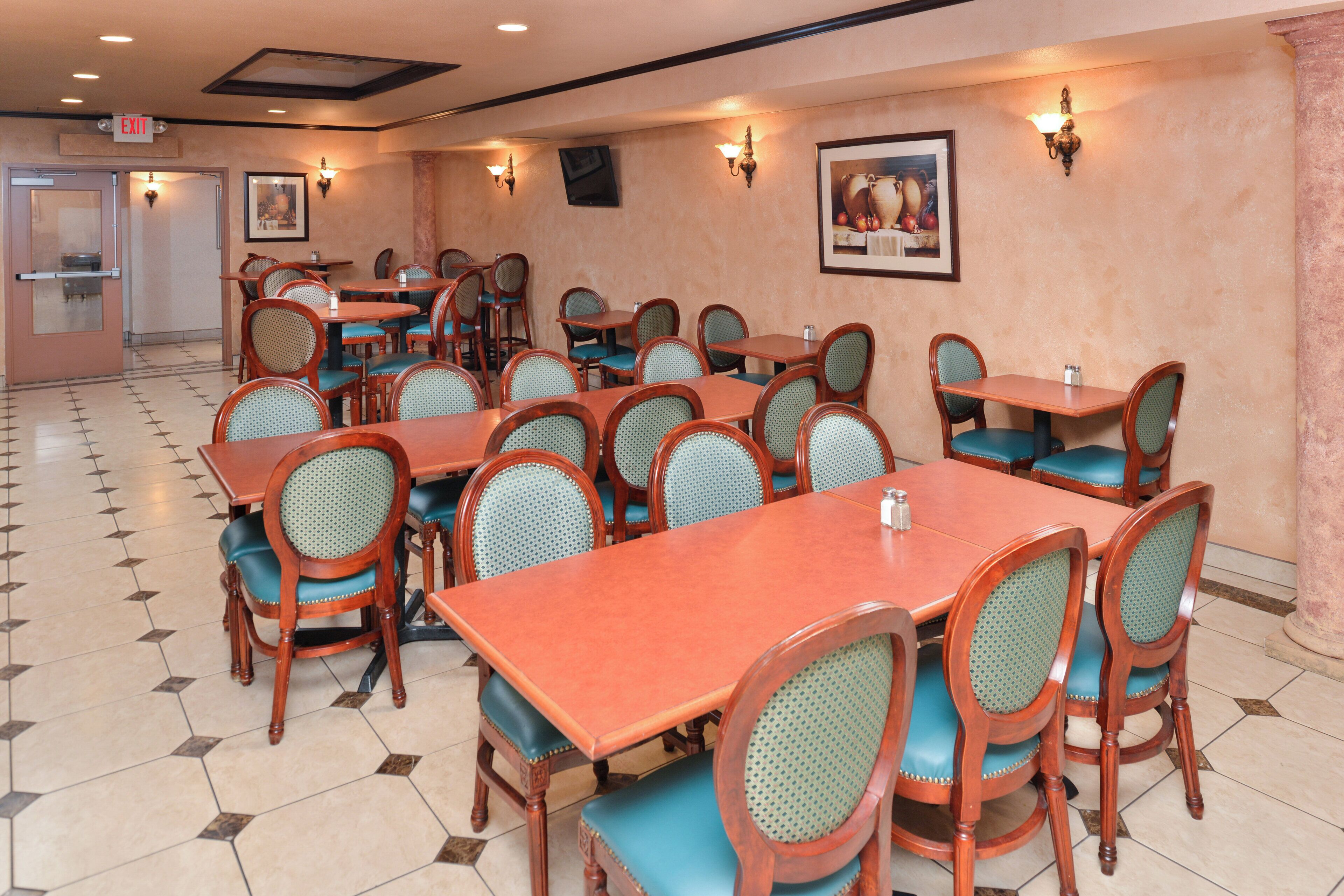 A restaurant with multiple tables and chairs, a tiled floor, and wall-mounted lighting.