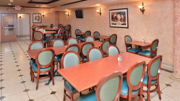 A restaurant with multiple tables and chairs, a tiled floor, and wall-mounted lighting.