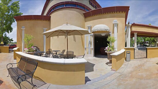 An outdoor patio area with a round table and chairs, a large umbrella, and potted plants. - Holiday Inn Rancho Cordova by IHG (Rancho Cordova)