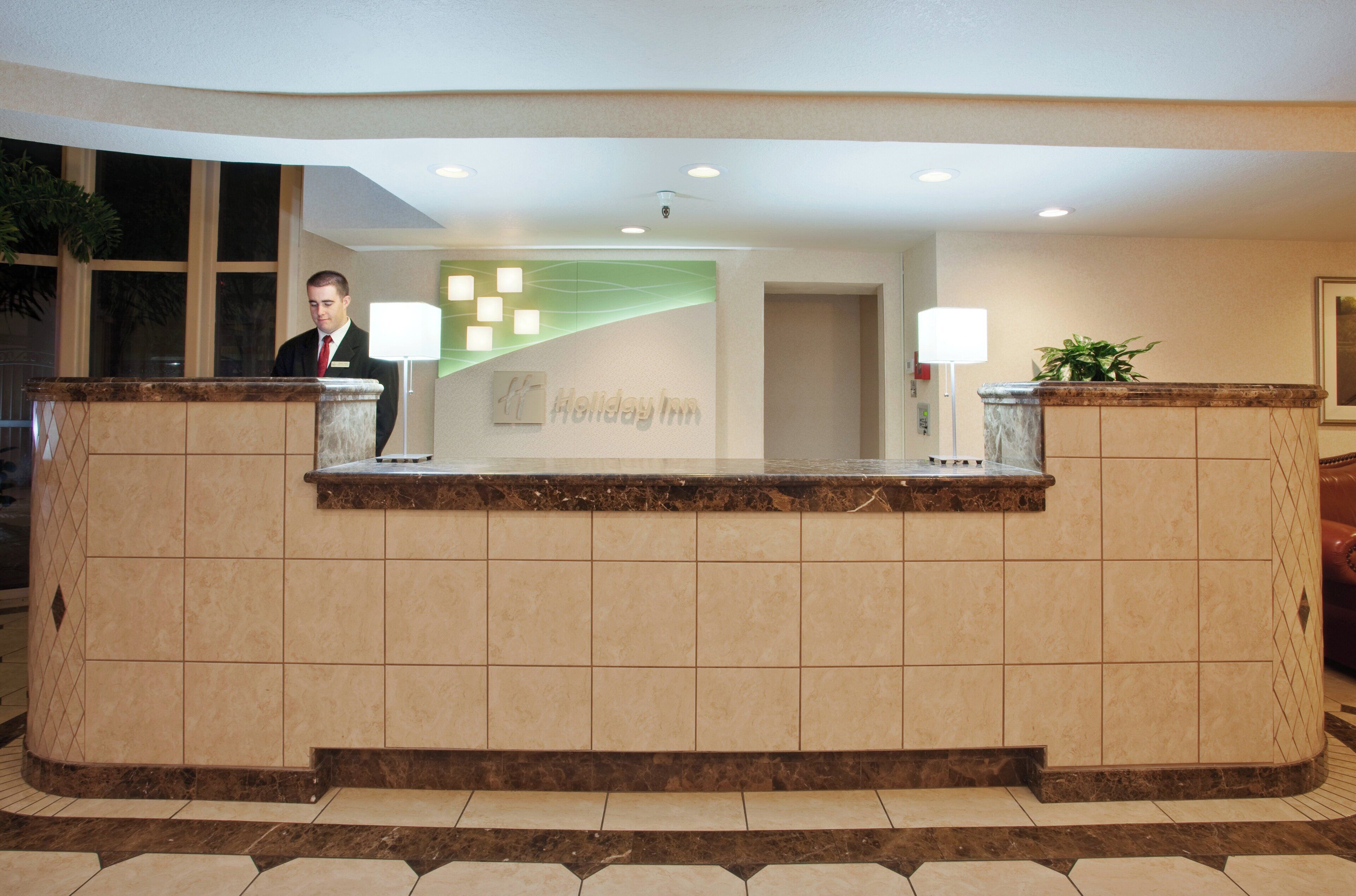 A reception desk with a nameplate, a plant, and a lamp.