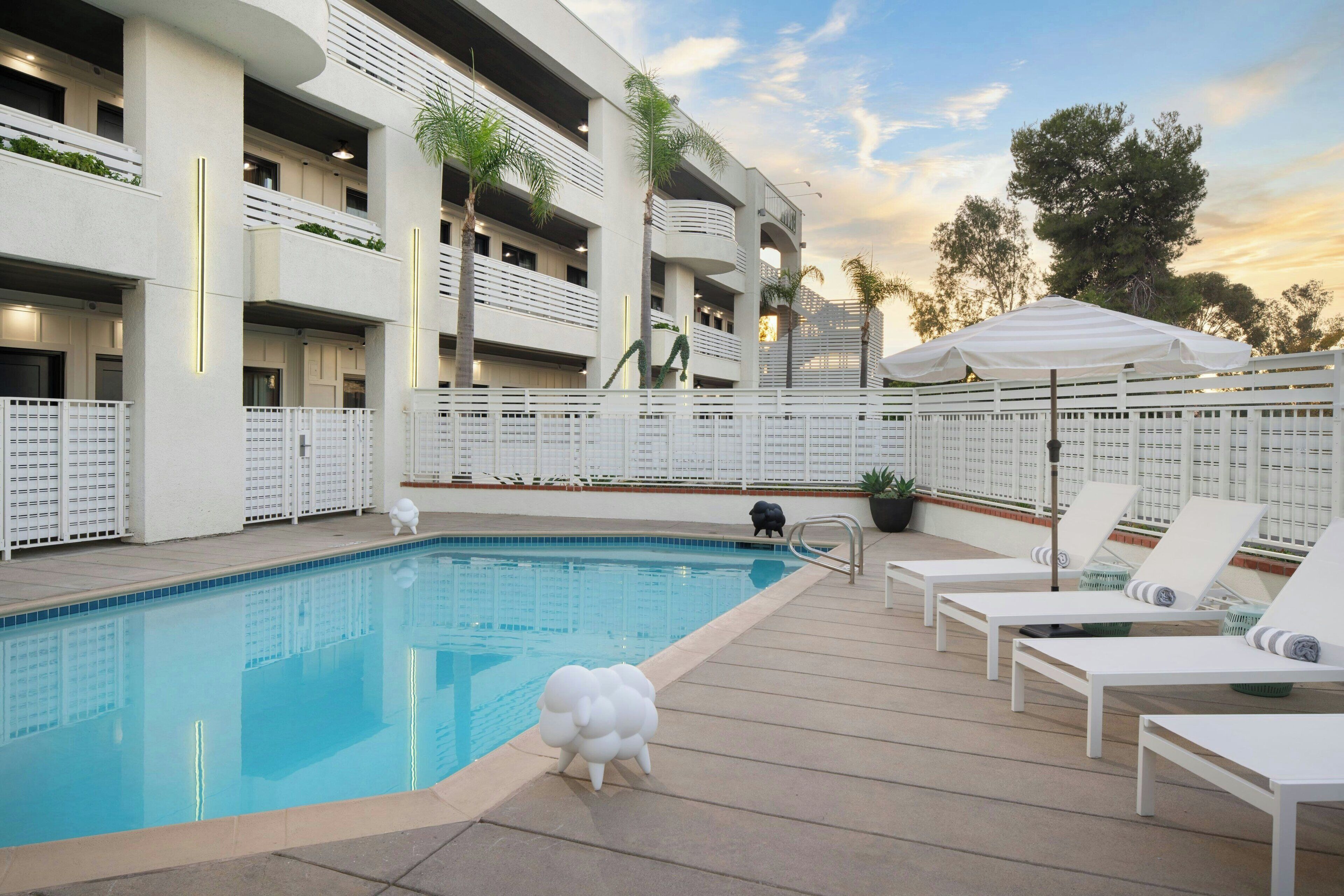 Un área de piscina con sillones de descanso, una pequeña estatua y un edificio con balcones.