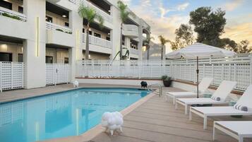 Un área de piscina con sillones de descanso, una pequeña estatua y un edificio con balcones.