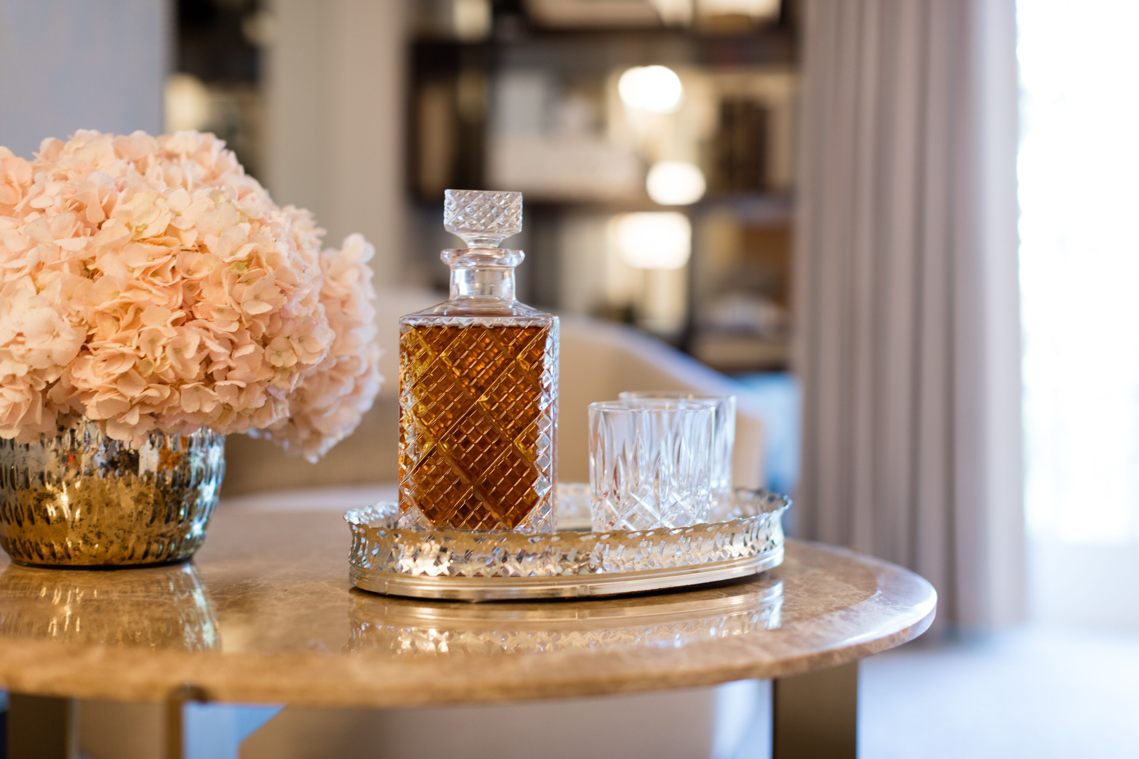 A table with a crystal decanter, a glass, and a bowl of pink flowers.