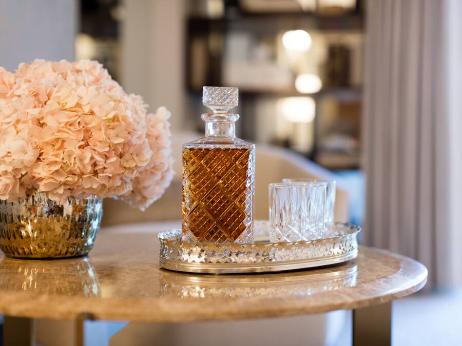 A table with a crystal decanter, a glass, and a bowl of pink flowers.