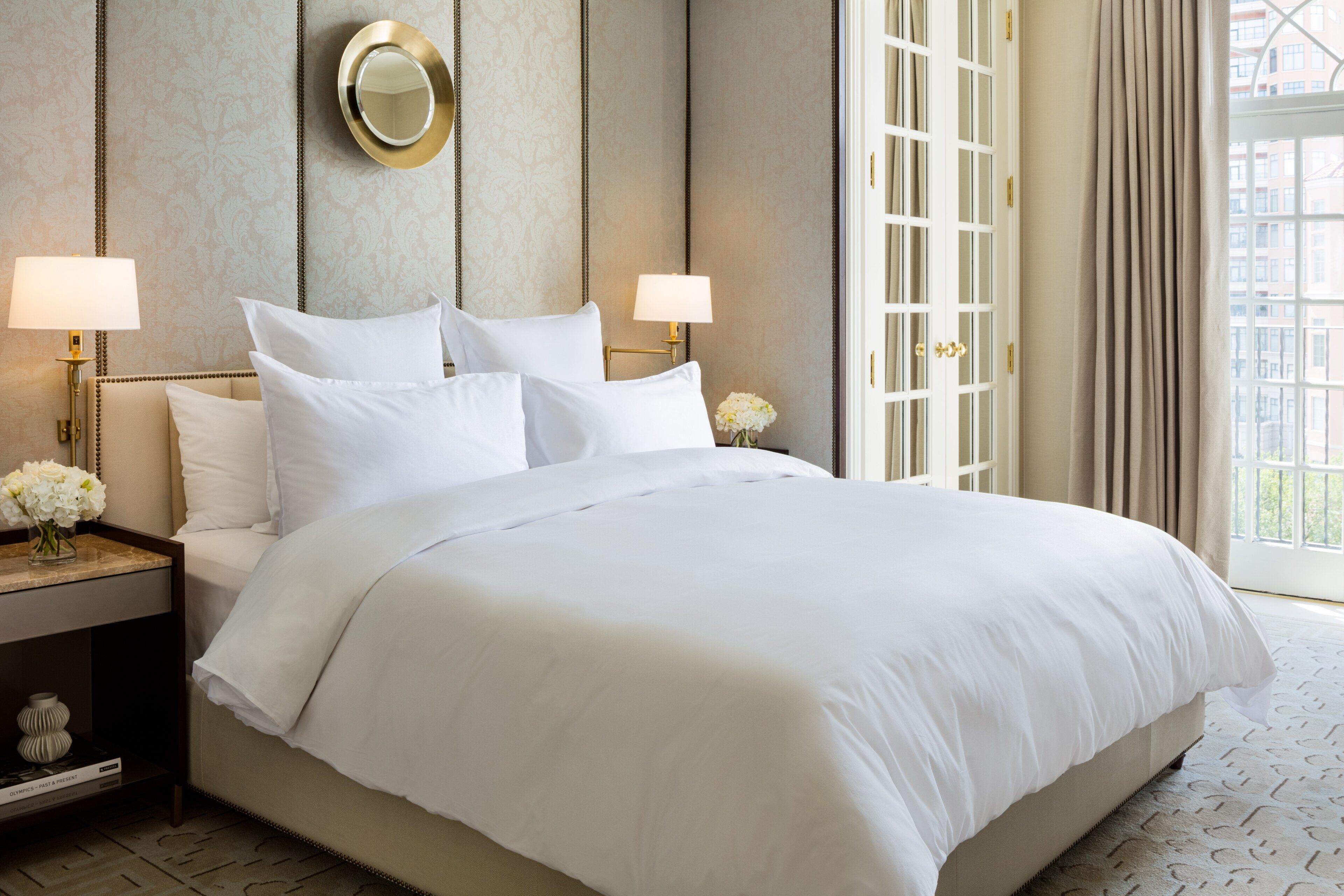 A hotel room with a large bed, two bedside lamps, a mirror, and a window with curtains.