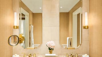 Un baño con dos lavamanos, grifos dorados, un espejo y un florero con flores.