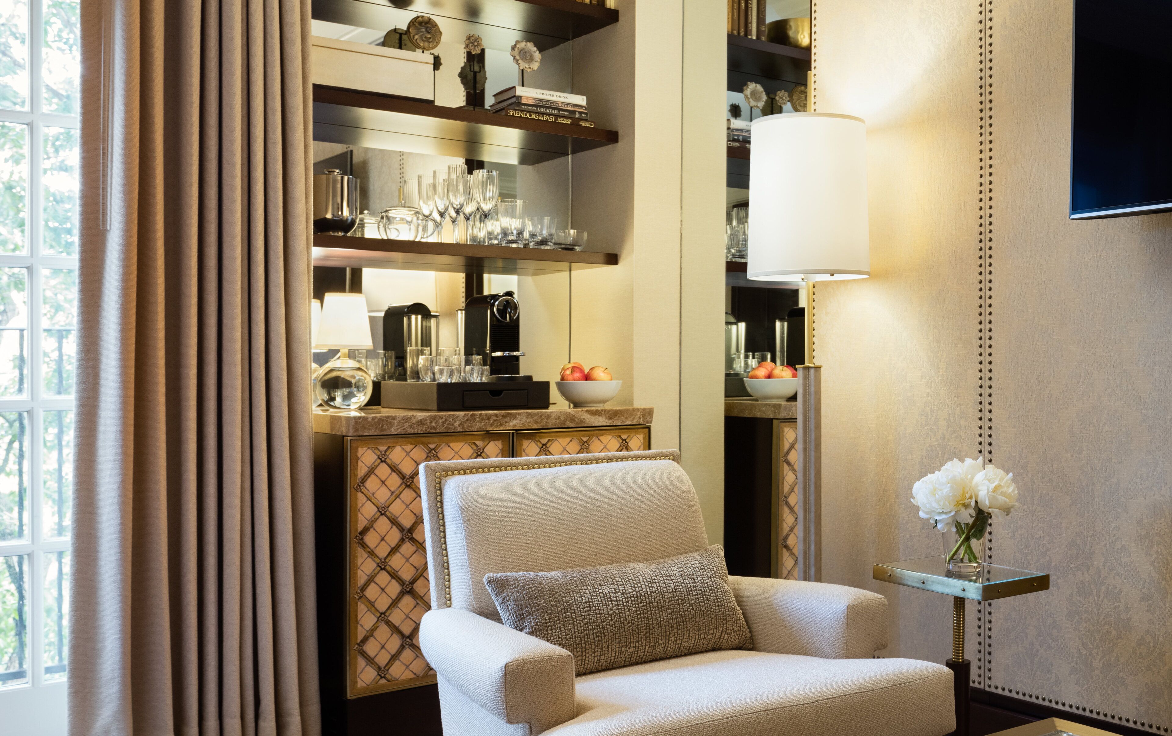 A well-lit room with a comfortable armchair, a coffee table with a bowl of fruit, and a shelf with books and decorative items.