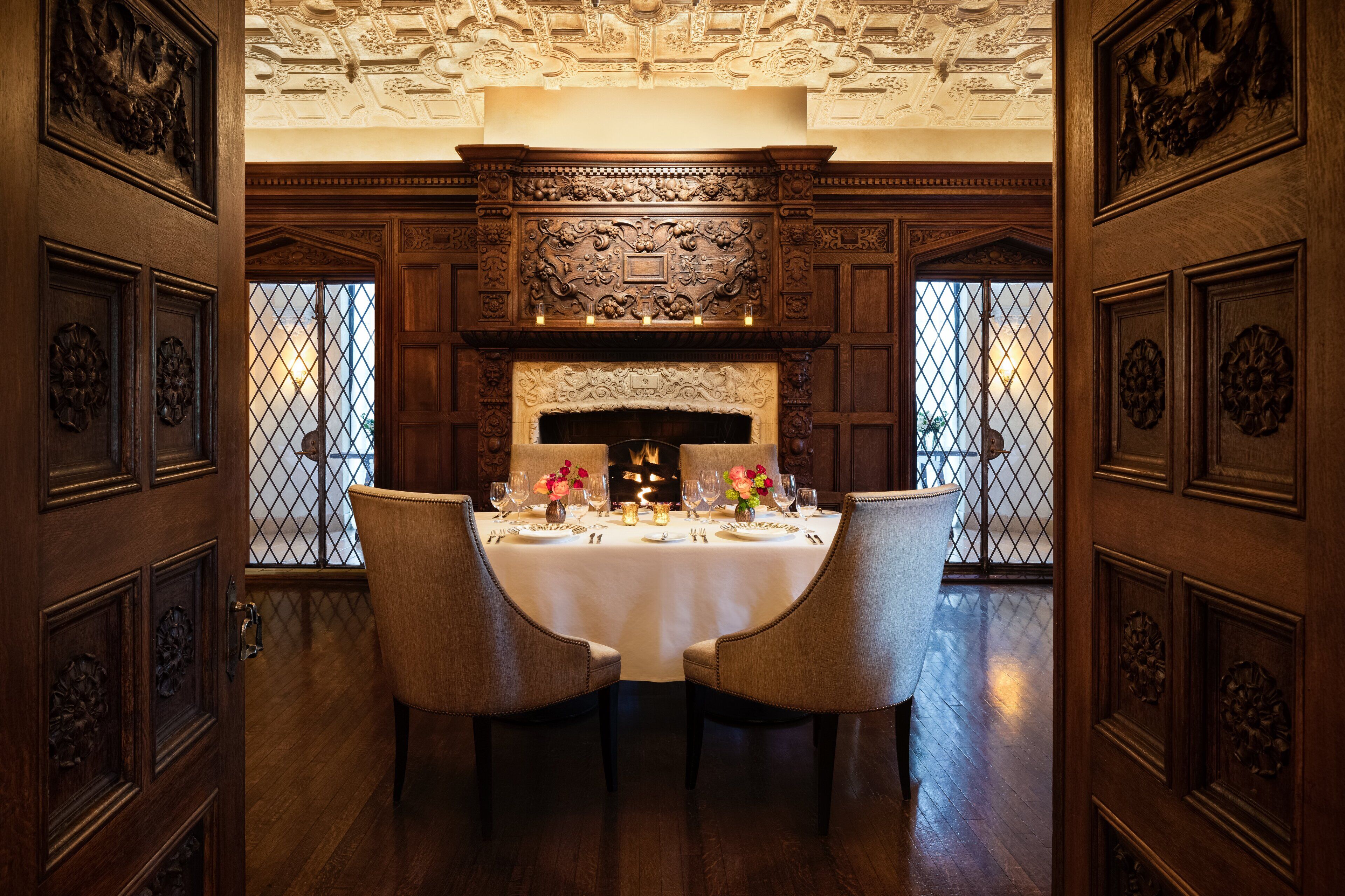 A dining room with a large wooden table set for four, surrounded by ornate wooden paneling and a decorative ceiling.