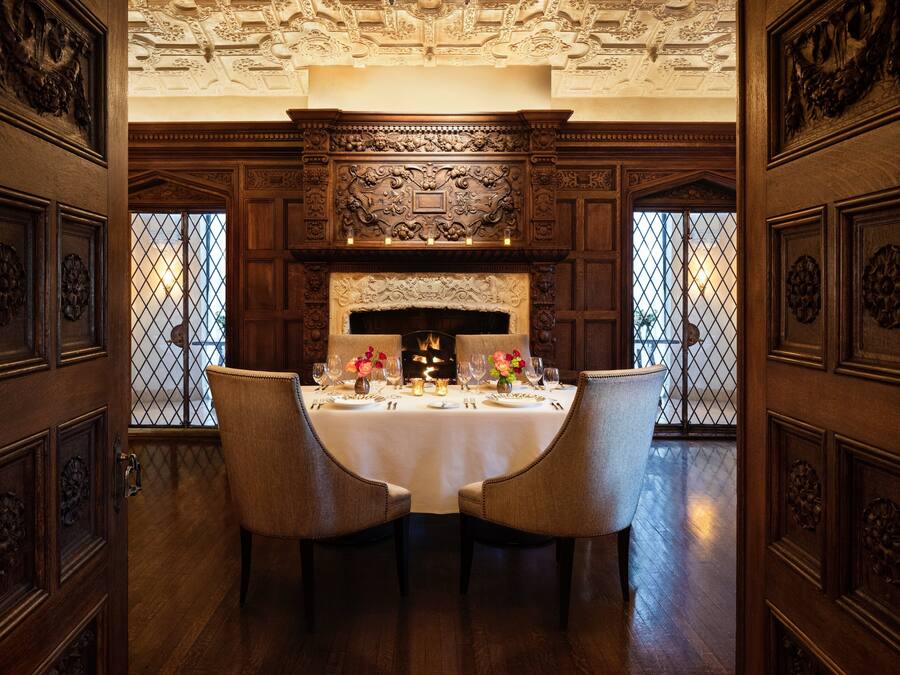 A dining room with a large wooden table set for four, surrounded by ornate wooden paneling and a decorative ceiling.