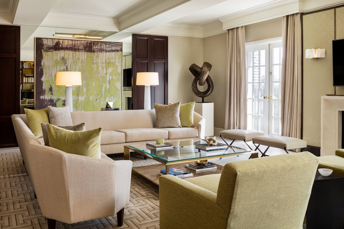Un salon moderne avec un canapé beige, des fauteuils verts, une table basse en verre et une cheminée.