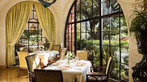 A dining area with tables set for a meal, large windows with curtains, and a chandelier. - Rosewood Mansion on Turtle Creek (Dallas)