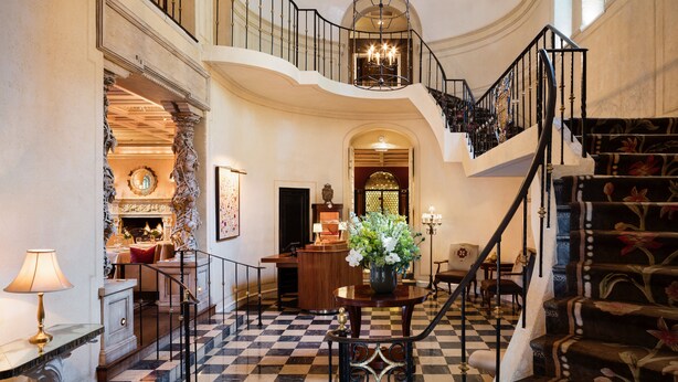 A grand lobby with a checkered floor, a staircase with floral carpet, and a chandelier. - Rosewood Mansion on Turtle Creek (Dallas)