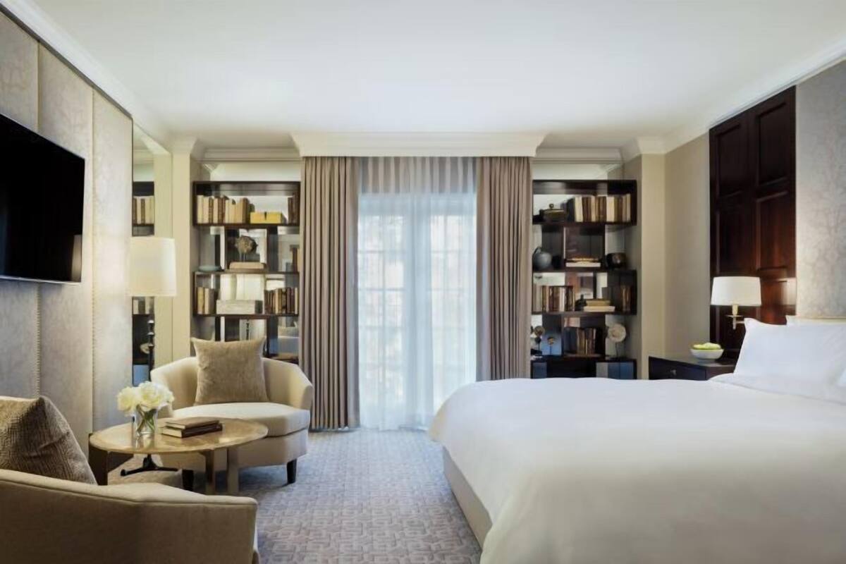 Une chambre d’hôtel comprenant un lit, un canapé, une petite table avec un vase, une bibliothèque et un téléviseur.